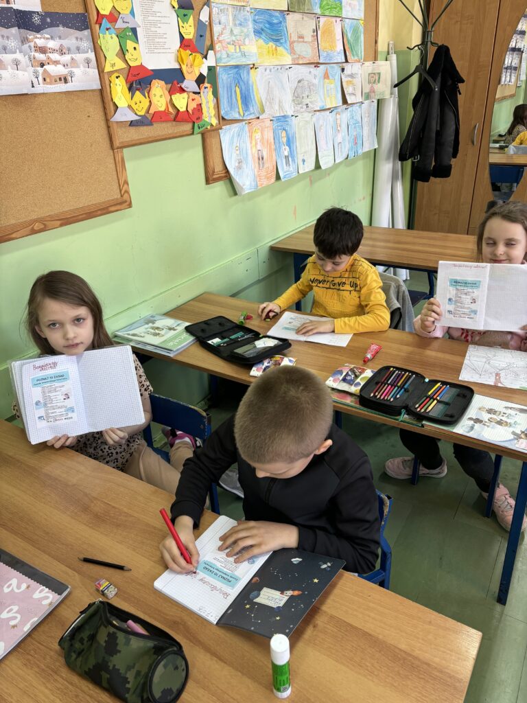 dzieci trzymają zeszyty z wklejonymi ulotkami z 10 zasadami bezpiecznego Internetu