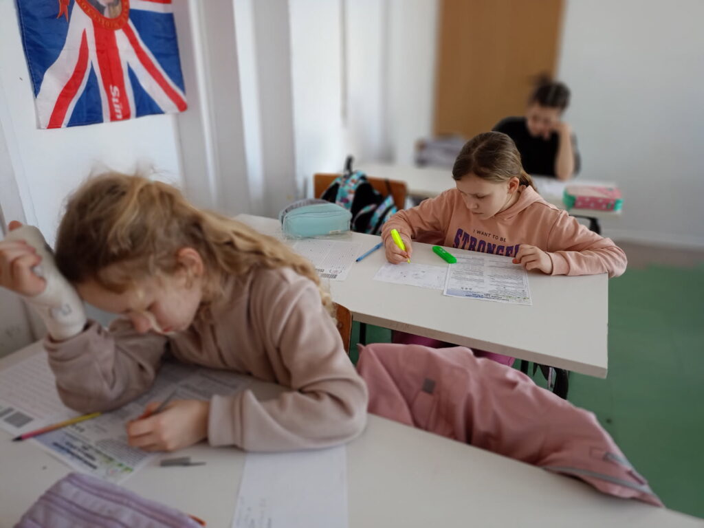 uczniowie siedzą przy ławkach z kartami zadań i rozwiązują zadania konkursowe