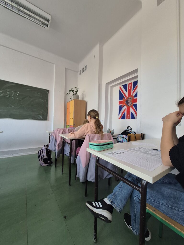 uczniowie siedzą przy ławkach z kartami zadań i rozwiązują zadania konkursowe