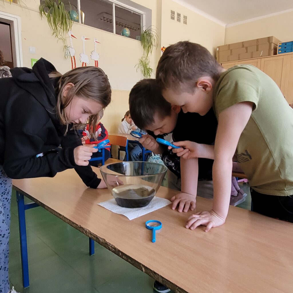 dzieci obserwują przez lupę eksperymenty