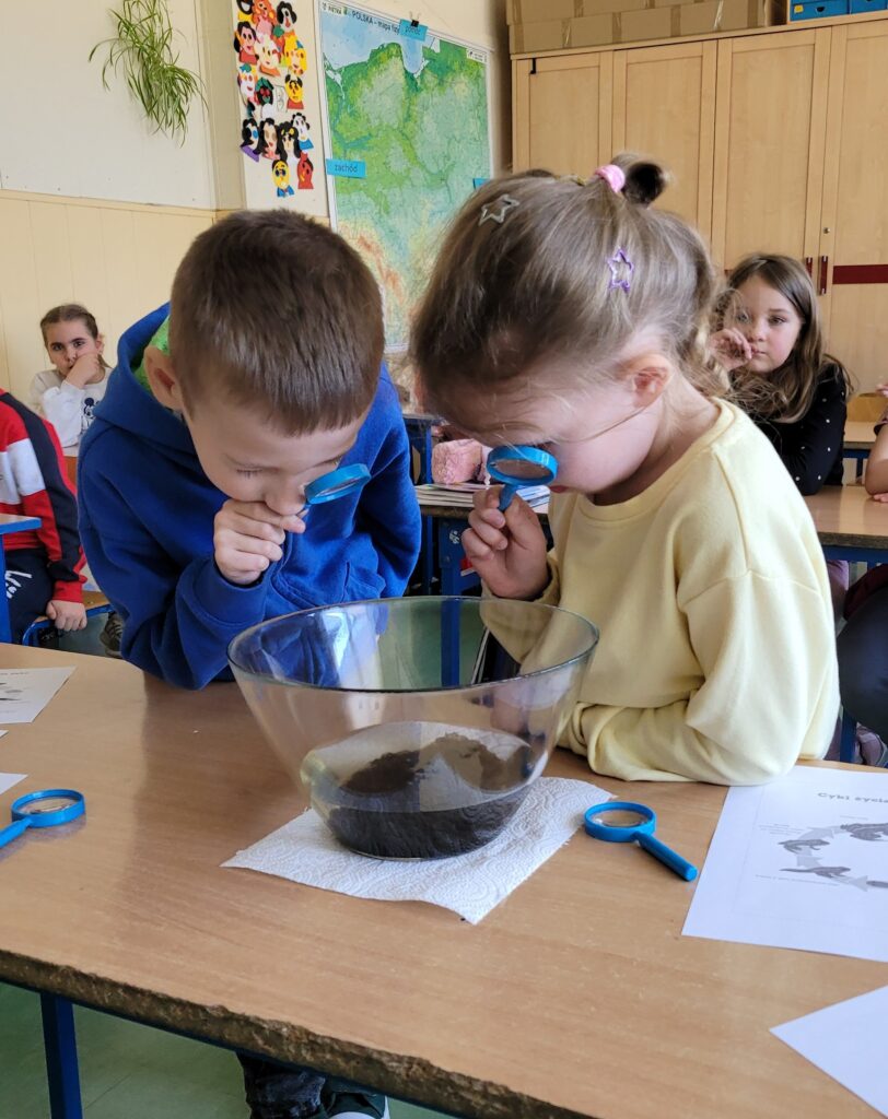 dzieci obserwują przez lupę eksperymenty