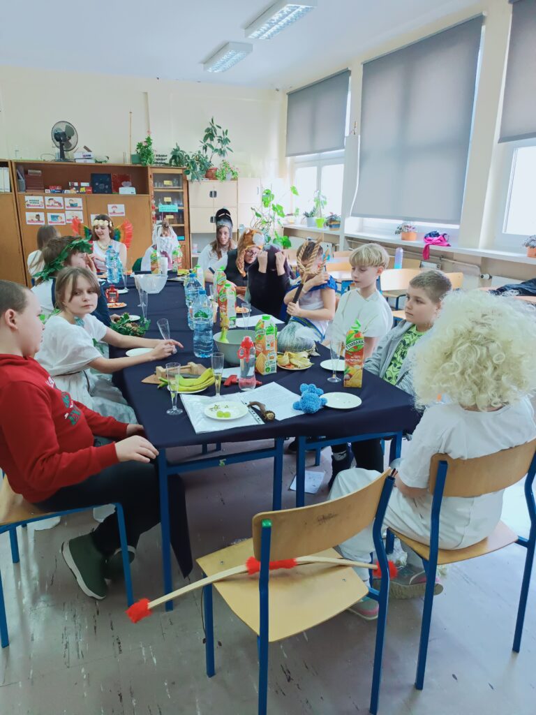 zdjęcie przedstawia uczniów siedzących przy ławkach nakrytych niebieskim obrusem i łakociami
