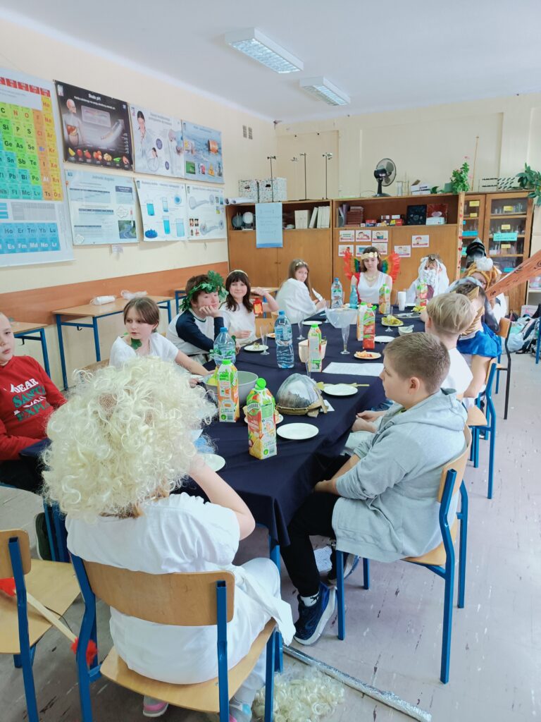 zdjęcie przedstawia uczniów siedzących przy ławkach nakrytych niebieskim obrusem i łakociami