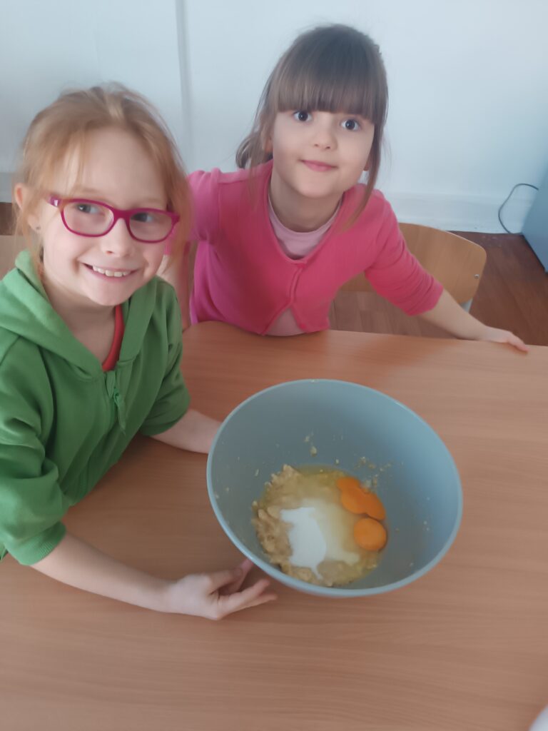 dziewczynki uśmiechają się , trzymają miskę ze wsypanymi składnikami