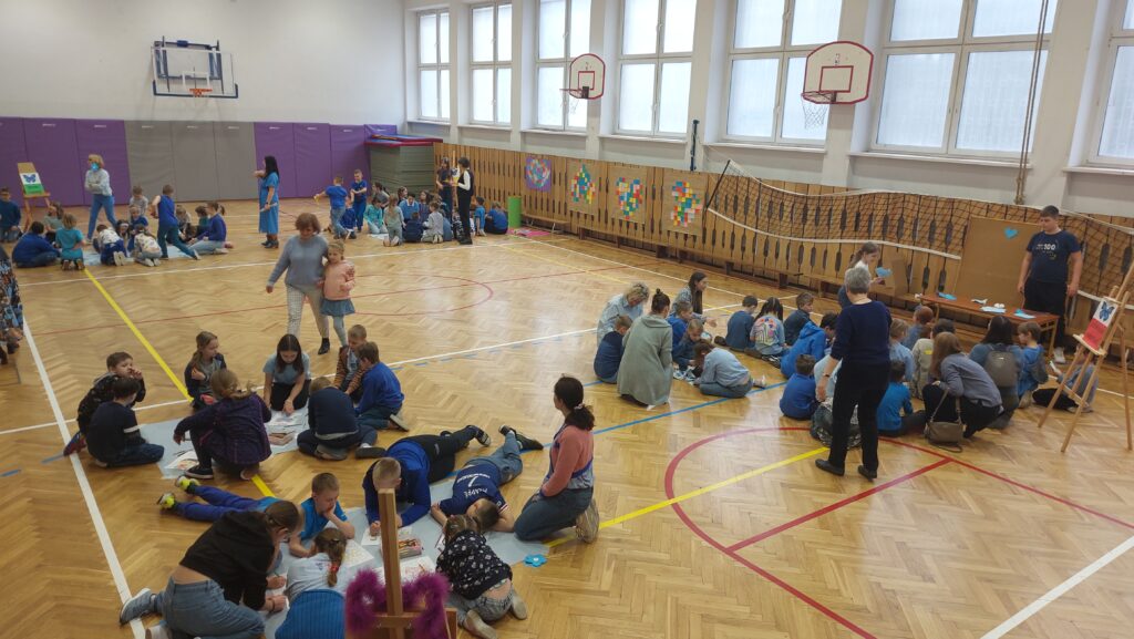 uczniowie siedzą na podłodze w sali gimnastycznej podzieleni na grupy, wykonują zadania