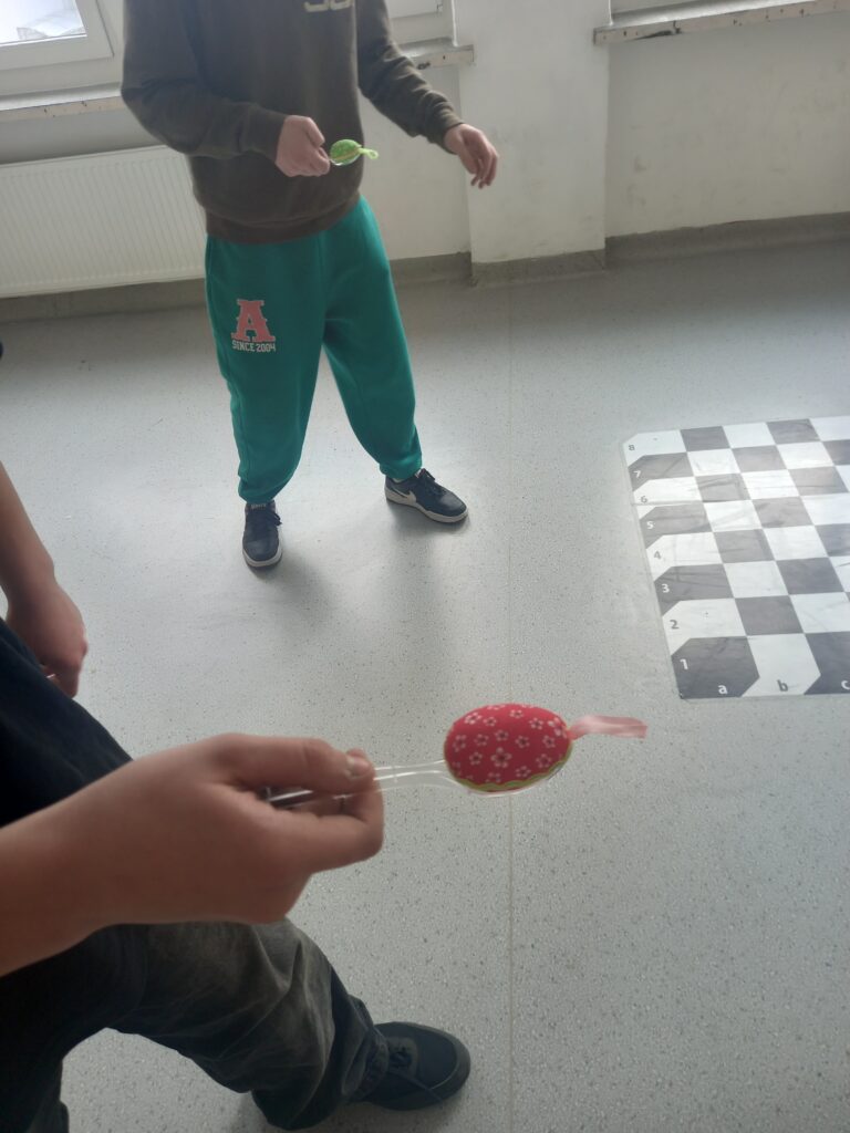 Dwóch uczniów trzyma na łyżkach po jednym kolorowym jajku na szkolnym korytarzu