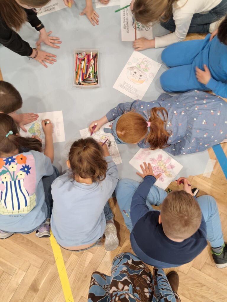 uczniowie wykonują karty pracy na niebieskim papierze siedząc