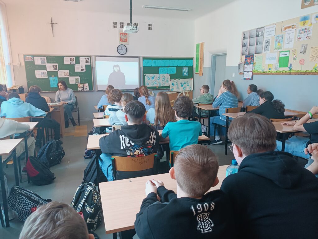 uczniowie siedzą w ławkach w niebieskich koszulkach, biorą udział w warsztatach edukacyjnych