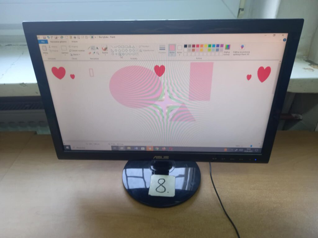 Monitor komputera z pracą dzieci różowymi figurami geometrycznymi i serduszkami