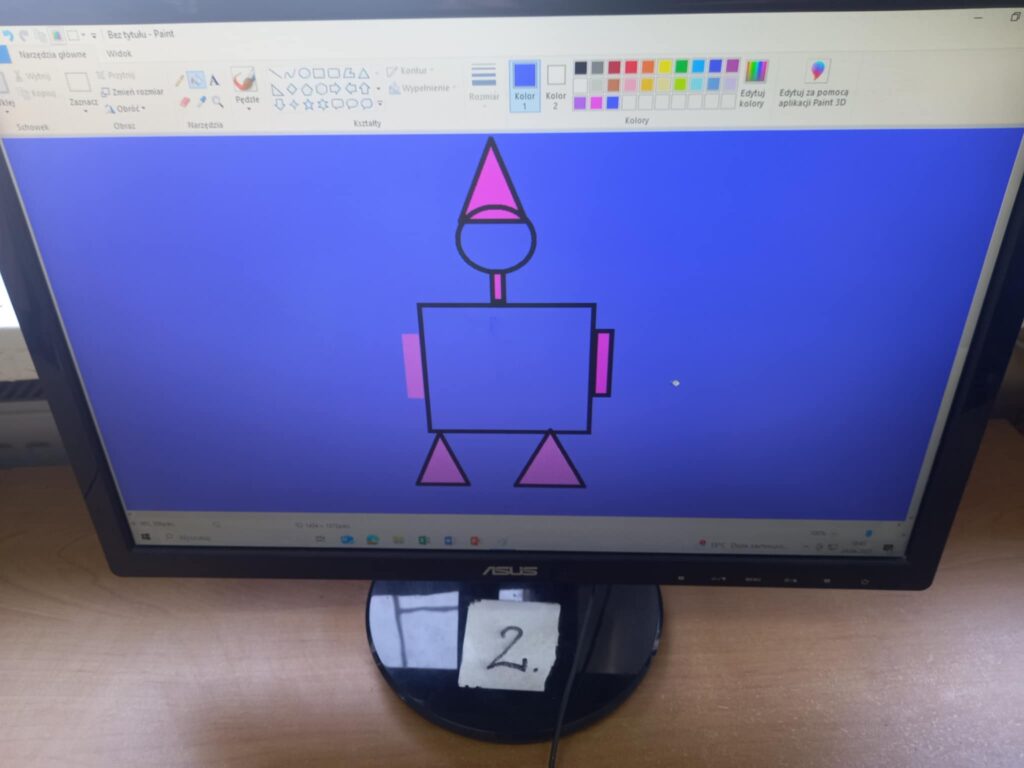 Monitor z pracą dzieci. Na niebieskim tle pajacyk z figur geometrycznych