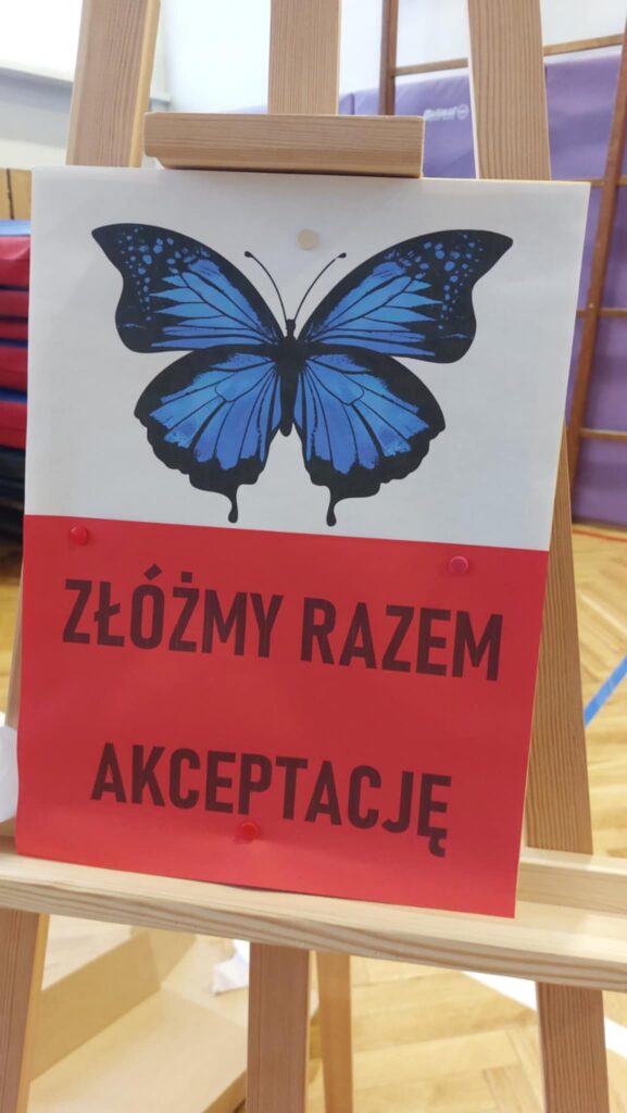 namalowany niebieski motyl pod ni na czerwonym tle czarny napis: złóżmy razem akceptację