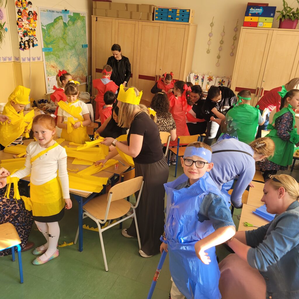 na zdjęciu widzimy uczniów i mamy w kolorowych strojach z papieru