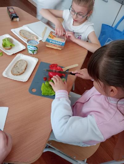 uczniowie kroją warzywa przy ławkach na deskach