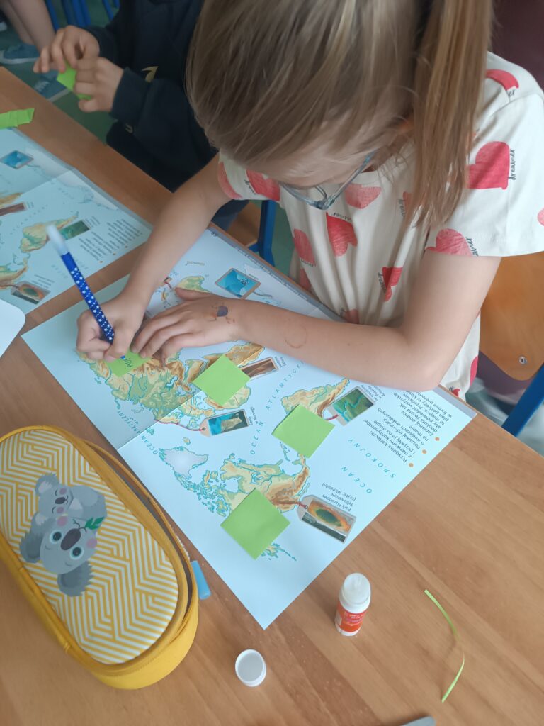 Uczennica pracuje przy biurku uzupełniając kartę pracy - mapę świata.