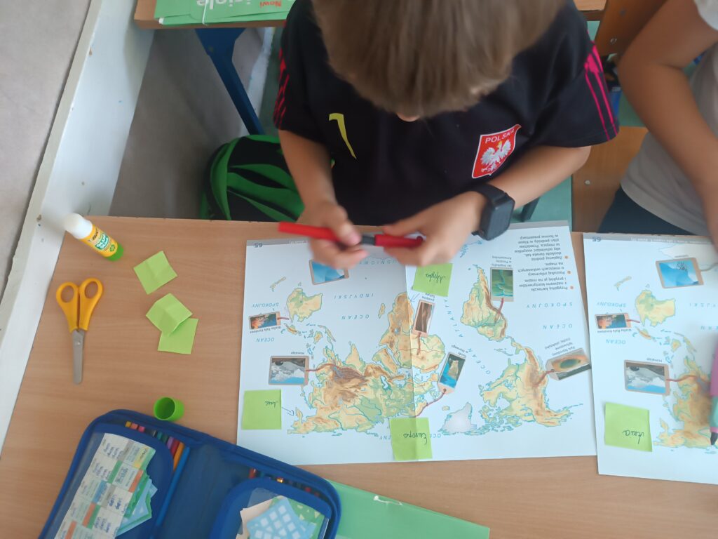 Uczeń pracuje przy biurku uzupełniając kartę pracy - mapę świata.