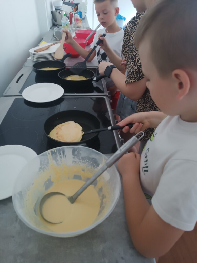 Uczeń samodzielnie przekłada naleśnika na patelni, dalej nauczycielka z innym uczniem stoi przy drugiej patelni.