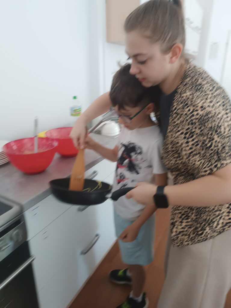 Nauczycielka pomaga uczniowi przewrócić naleśnika na drugą stronę.