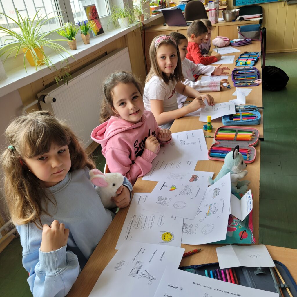 zdjęcie klasy, uczniowie siedzą w ławkach, obok stoi pani i wręcza kartki z zadaniami