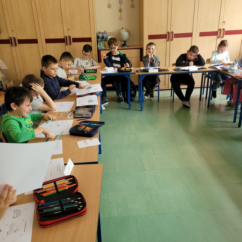 zdjęcie klasy, uczniowie siedzą w ławkach, obok stoi pani i wręcza kartki z zadaniami