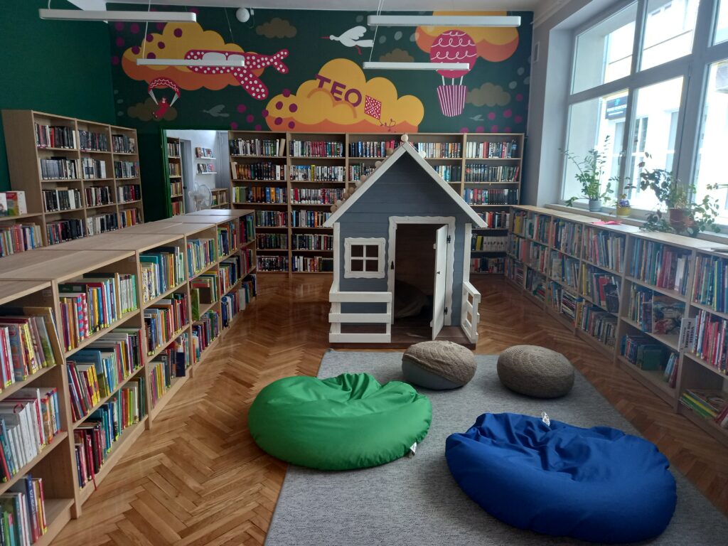 zdjęcie książek na półkach, po środku stoi domek do zabawy