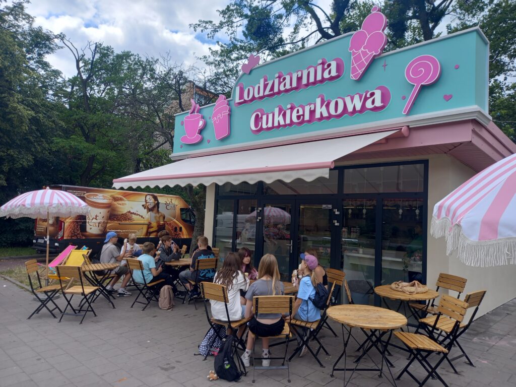 dzieci siedzą przy stoliku przy lodziarni i jedzą lody