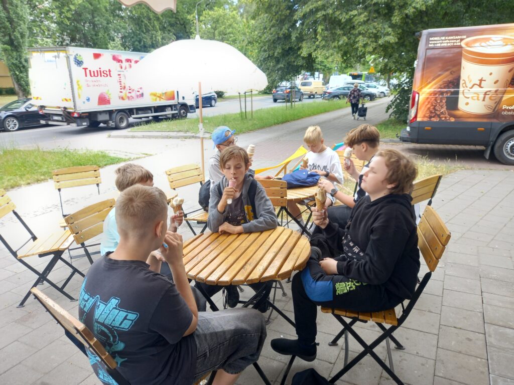 dzieci siedzą przy stoliku przy lodziarni i jedzą lody