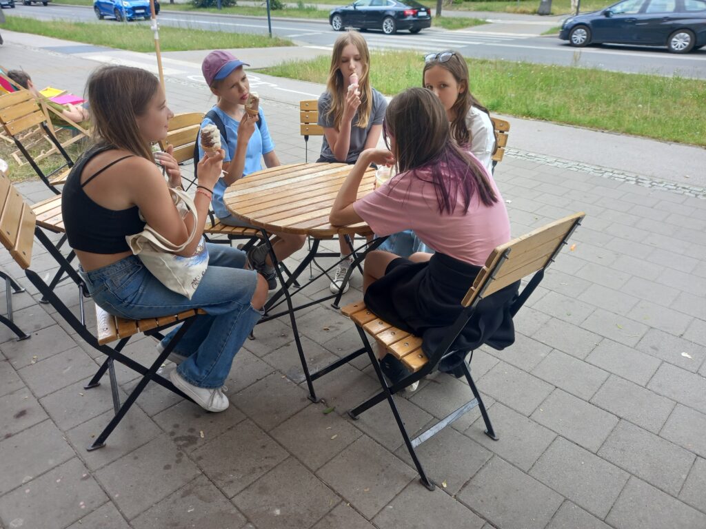 dzieci siedzą przy stoliku przy lodziarni i jedzą lody
