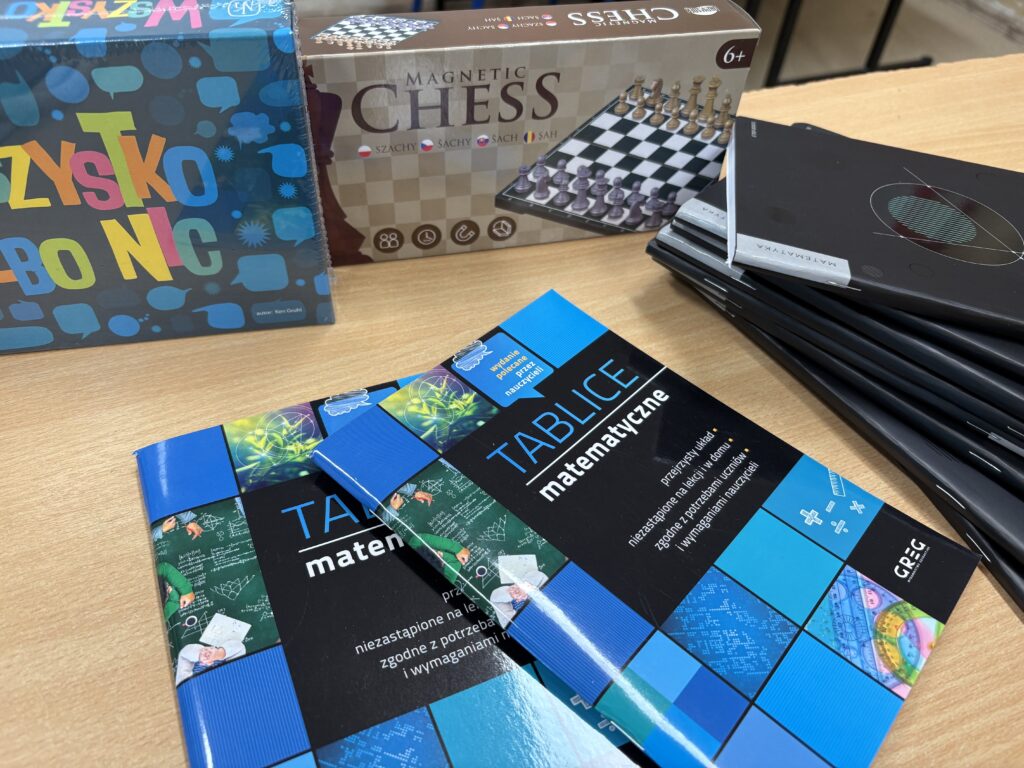 Dwie książki z napisem Tablice matematyczne, stos czarnych zeszytów, dwie gry w pudełkach: Wszystko albo nic i Chess