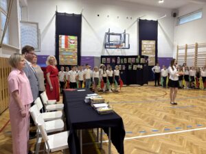 uczennica przemawia na środku sali, uczniowie i Dyrektorowie stoją na baczność