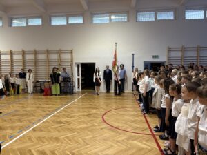 poczet sztandarowy, obok nauczyciel i pracownik szkoły. śpiewany hymn przez dzieci.