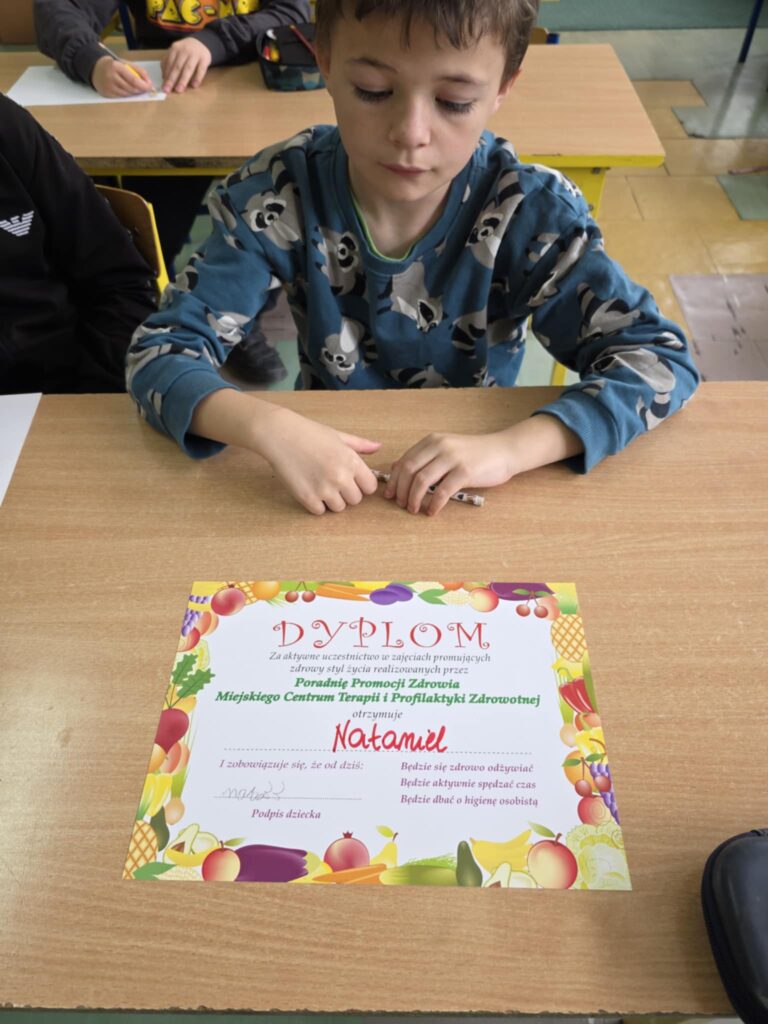 zdjęcie ucznia i dyplomu leżącego przed nim.