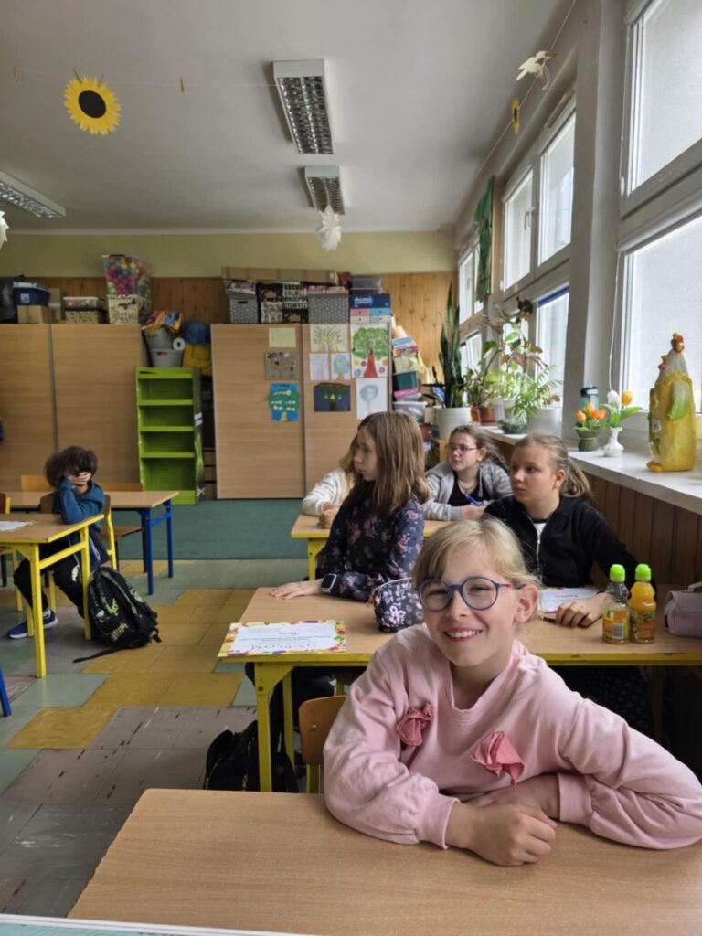 dzieci siedzą w ławkach uśmiechnięte podczas warsztatów