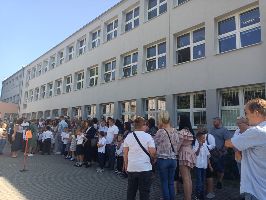 zdjęcie grupy uczniów z rodzicami i nauczycielami na apelu szkolnym przed szkołą