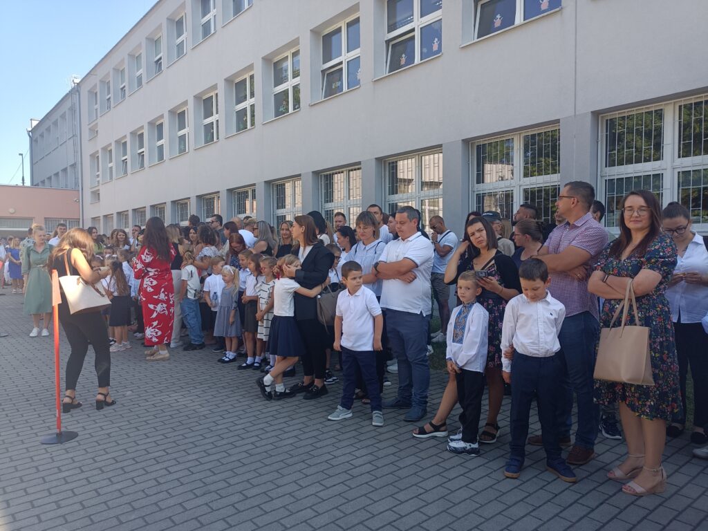 zdjęcie grupy uczniów z rodzicami i nauczycielami na apelu szkolnym przed szkołą
