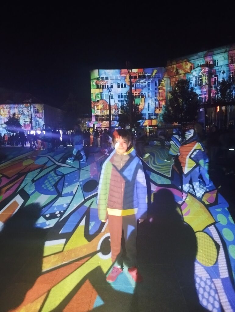 Artur z 6 c - chłopiec stoi na Placu Wolności na tle podświetlanych budynków