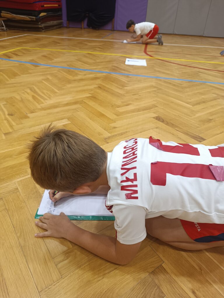 dzieci piszą na kartkach na podłodze w sali gimnastycznej
