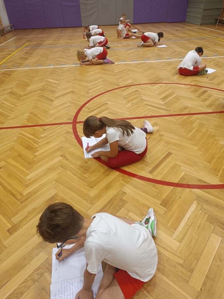dzieci piszą na kartkach na podłodze w sali gimnastycznej