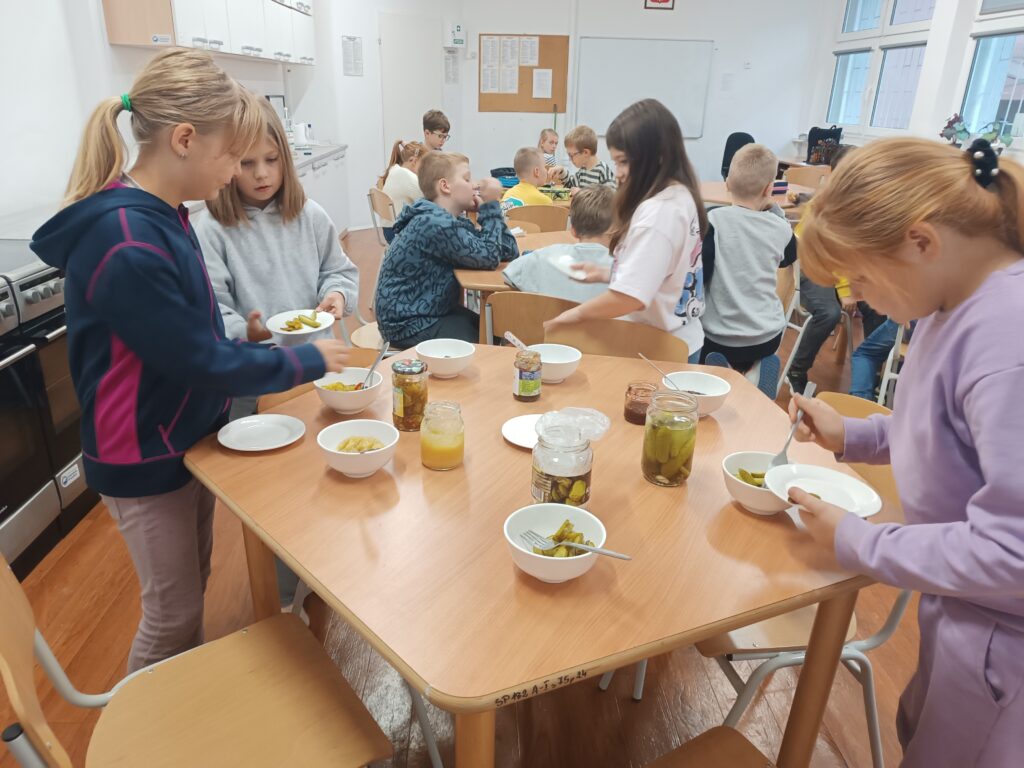 dzieci nakładają sobie produkty do spróbowania, niektórzy siedzą przy stolikach i próbują. 