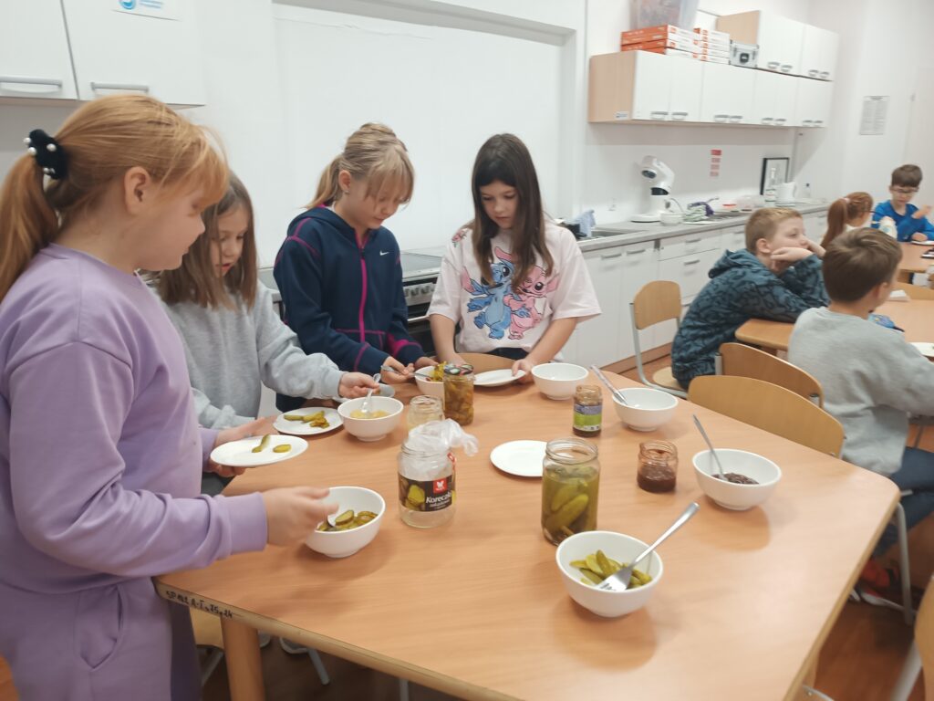 dzieci nakładają sobie produkty do spróbowania, niektórzy siedzą przy stolikach i próbują. 