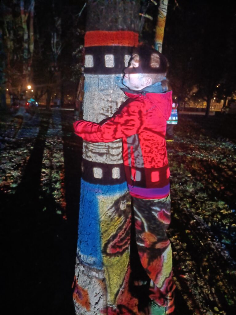 Szymon 6 a - chłopiec przytulony do drzewa, na nim puszczona kolorowa taśma