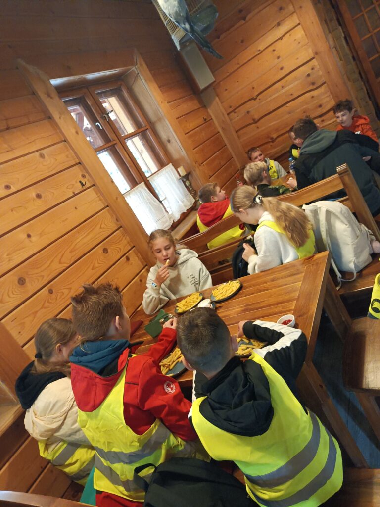 uczniowie siedzą przy stolikach i jedzą frytki. 