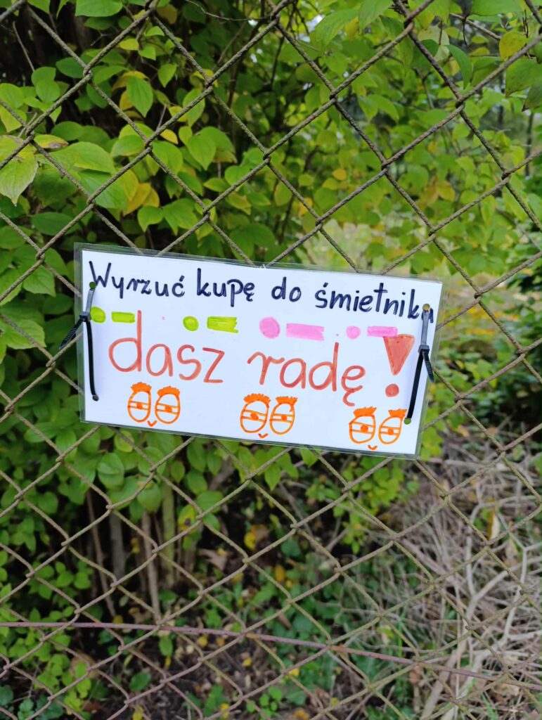 naklejona na płocie kartka z napisem wyrzuć kupę do śmietnika dasz radę