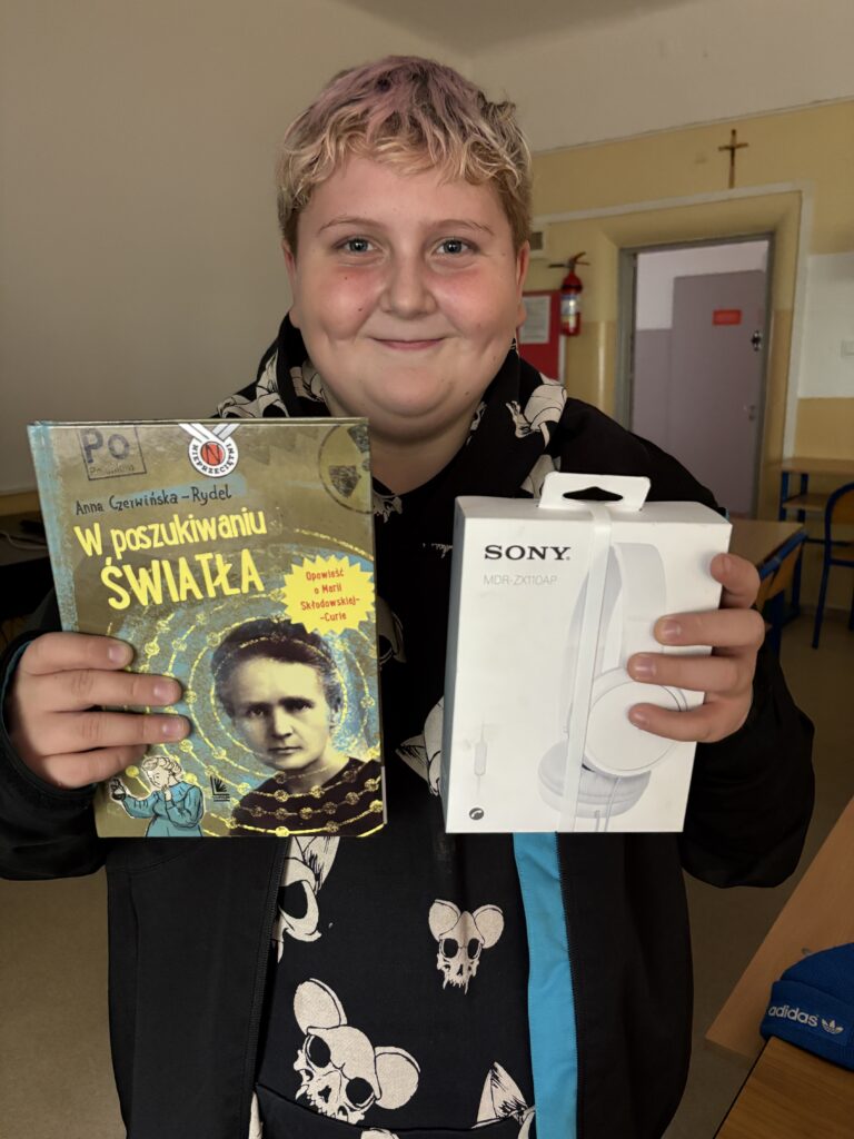 uczeń trzyma słuchawki i książkę - nagrodę.