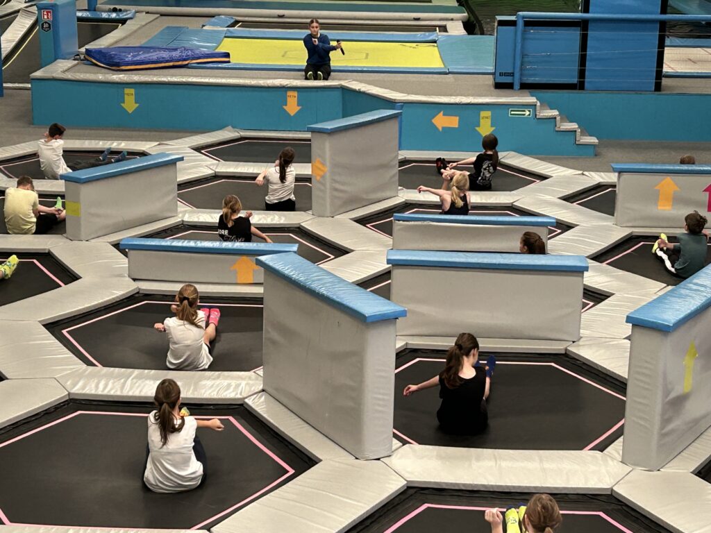 W parku trampolin dzieci ćwiczą, rozciągają się, mają rozgrzewkę