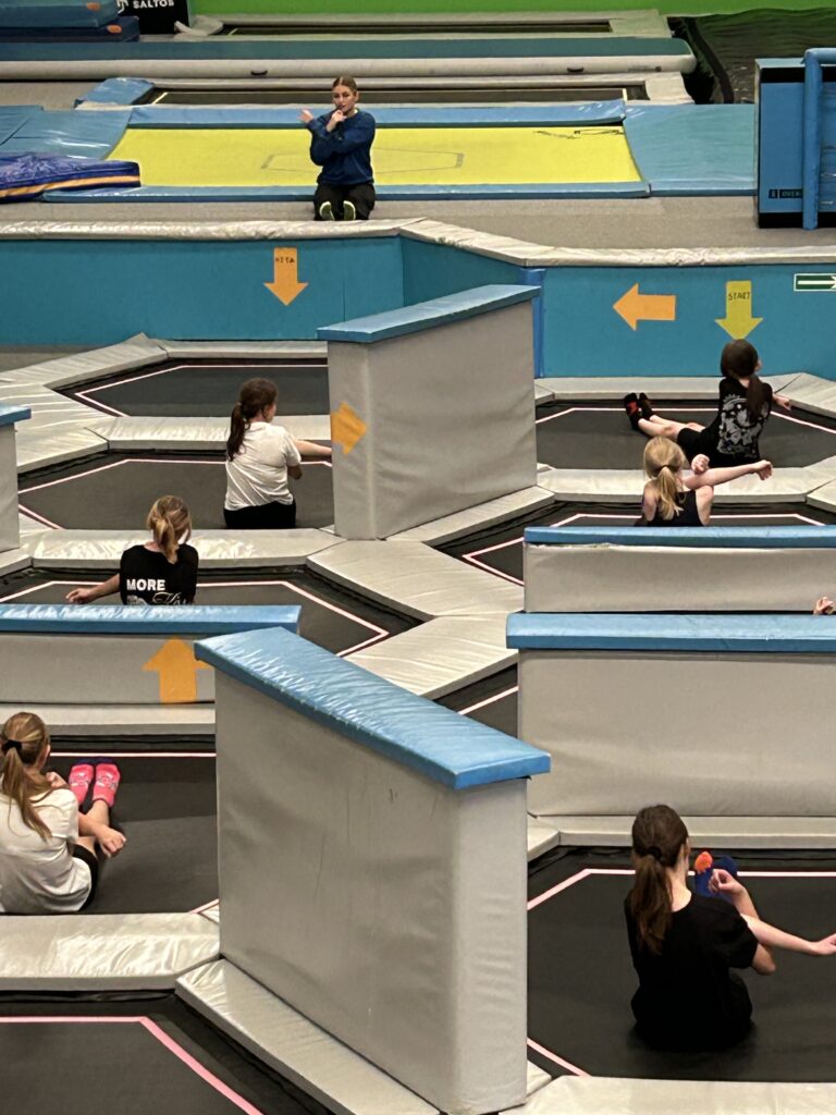 W parku trampolin dzieci ćwiczą, rozciągają się, mają rozgrzewkę