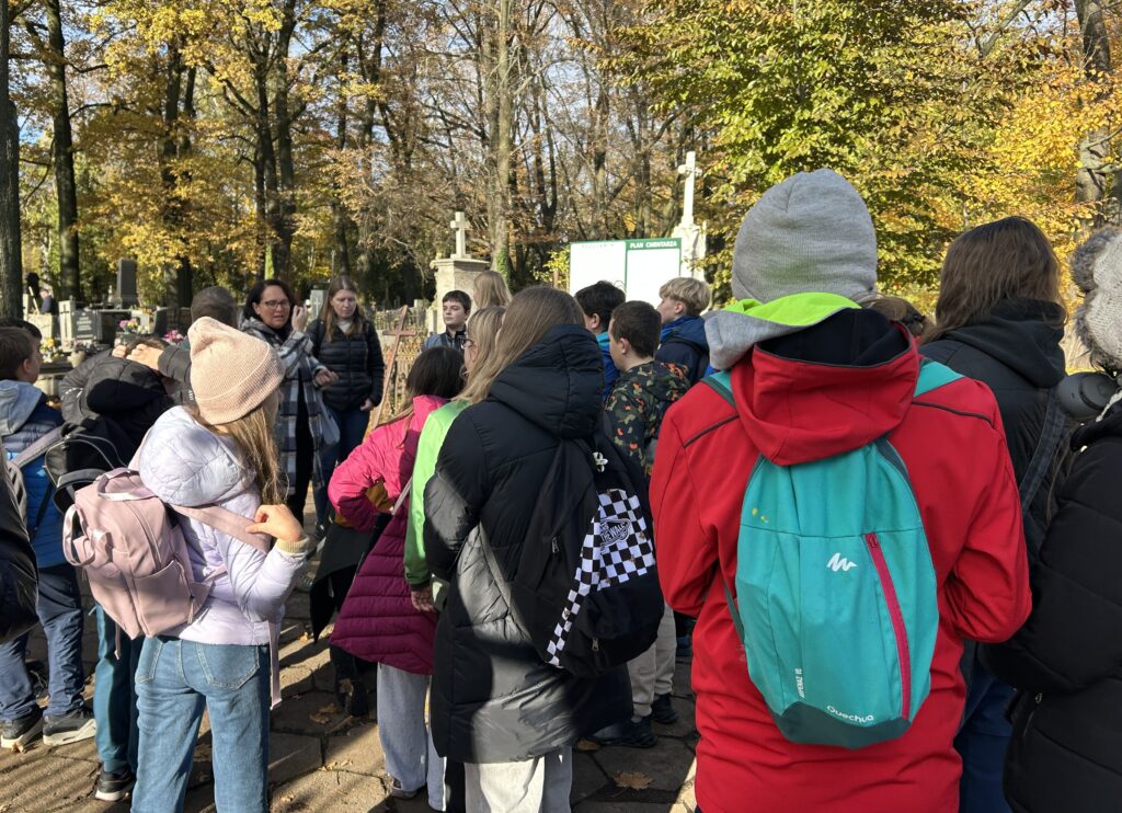 dzieci stoją tyłem do aparatu, pani opowiada im o miejscu,