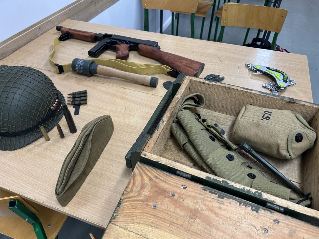 na ławce wyłożone eksponaty: hełm, furażerka, granat, karabin, skrzynka wojskowa a w niej pas na naboje, menażka