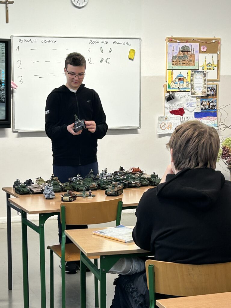 w klasie na lekcji, chłopiec prezentuje pojazdy wojskowe z klocków