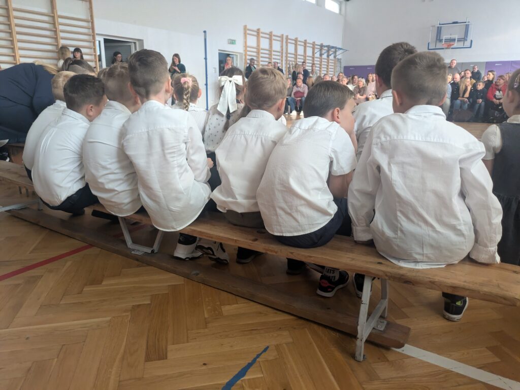 zdjęcie uczniów od tyłu, siedzą na ławeczkach