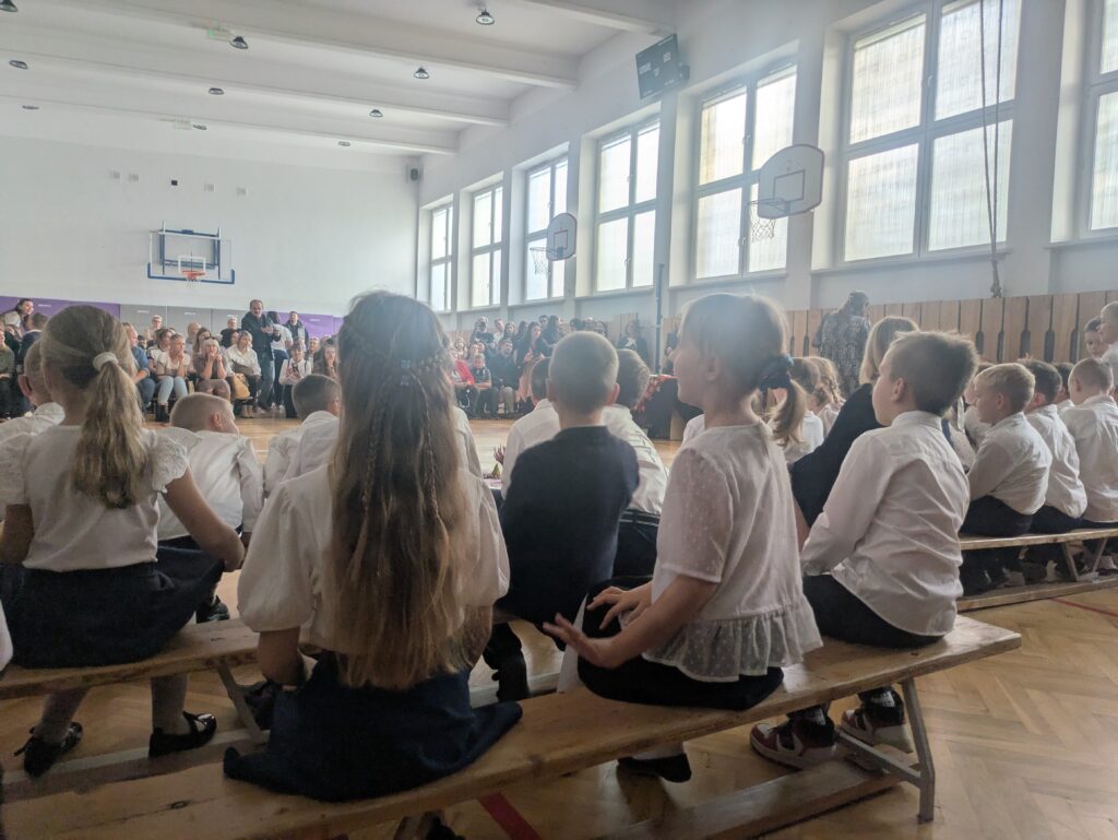 zdjęcie uczniów od tyłu, siedzą na ławeczkch